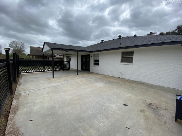 back of property with a patio area, roof with shingles, fence, and brick siding