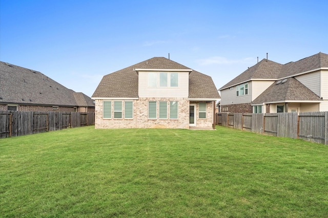 back of house featuring brick siding, a fenced backyard, a shingled roof, and a yard