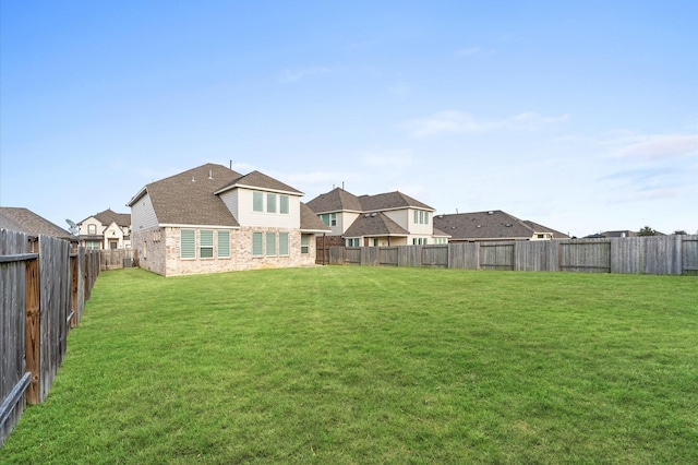 back of property featuring a fenced backyard, a lawn, and brick siding