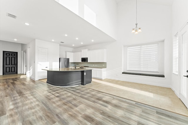 kitchen featuring a kitchen island with sink, visible vents, white cabinets, freestanding refrigerator, and light wood finished floors