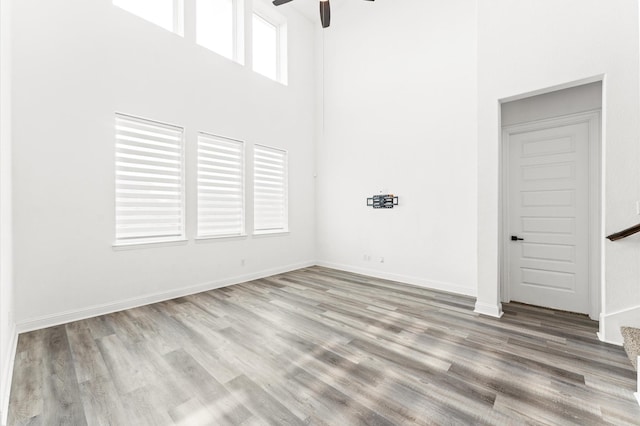 spare room with a ceiling fan, baseboards, a high ceiling, and wood finished floors