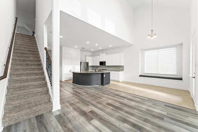 kitchen with light wood-style flooring, white cabinets, freestanding refrigerator, an island with sink, and an inviting chandelier