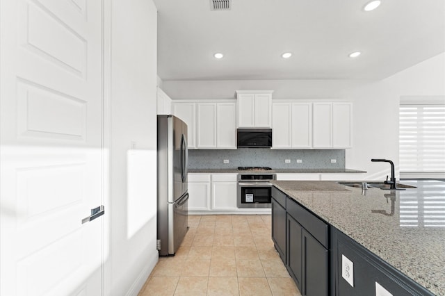 kitchen featuring tasteful backsplash, stainless steel appliances, white cabinetry, a sink, and light tile patterned flooring