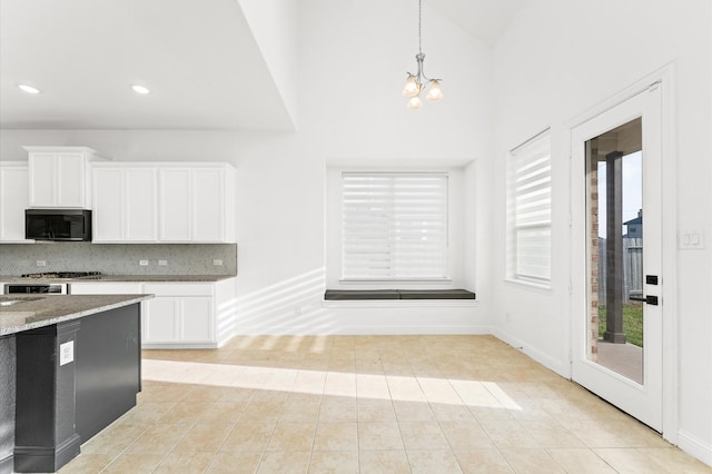 kitchen with black microwave, light tile patterned floors, white cabinets, decorative backsplash, and light stone countertops