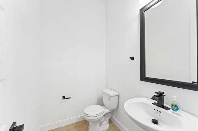 half bathroom with toilet, baseboards, a sink, and tile patterned floors