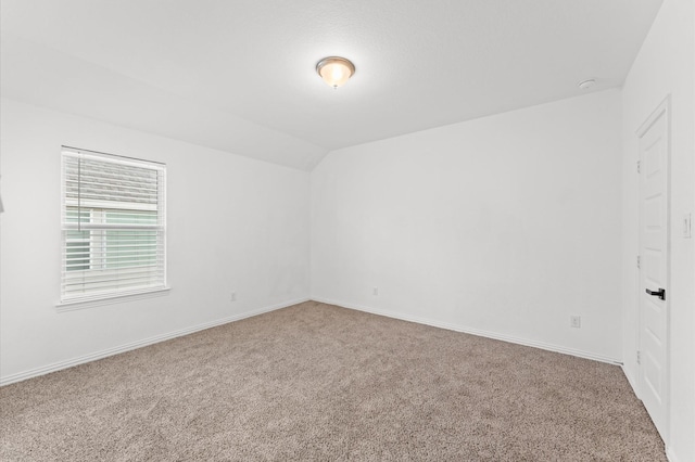 carpeted spare room with lofted ceiling and baseboards