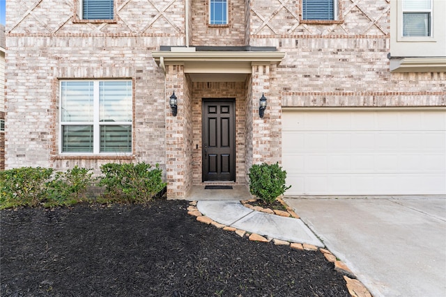 view of exterior entry with an attached garage, concrete driveway, and brick siding