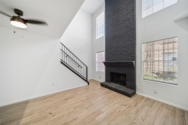 unfurnished living room featuring wood finished floors, baseboards, a high ceiling, stairs, and a brick fireplace