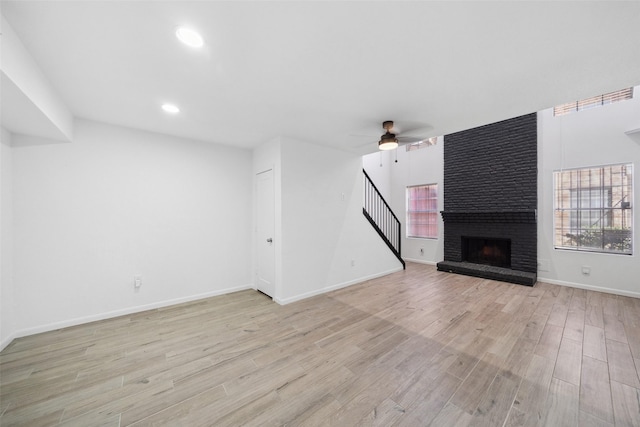 unfurnished living room featuring ceiling fan, baseboards, stairway, a fireplace, and light wood-style floors