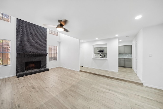 unfurnished living room with visible vents, a brick fireplace, light wood-type flooring, and ceiling fan