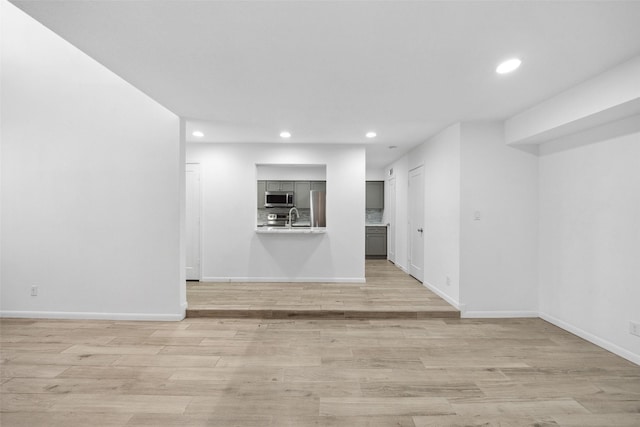 spare room with recessed lighting, baseboards, light wood finished floors, and a sink