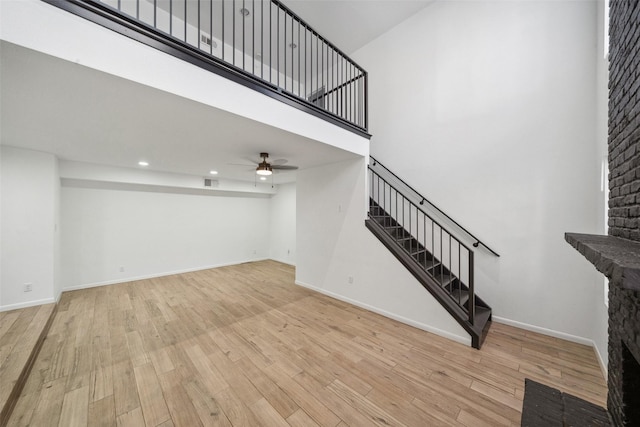 unfurnished living room with visible vents, baseboards, stairway, light wood-type flooring, and a high ceiling