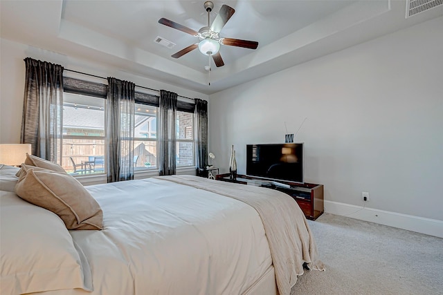 carpeted bedroom featuring baseboards, visible vents, a raised ceiling, and a ceiling fan