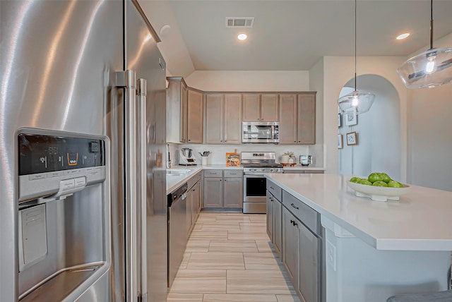 kitchen with a center island, stainless steel appliances, light countertops, visible vents, and hanging light fixtures