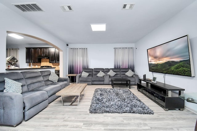 living room featuring light wood-style flooring, visible vents, and arched walkways