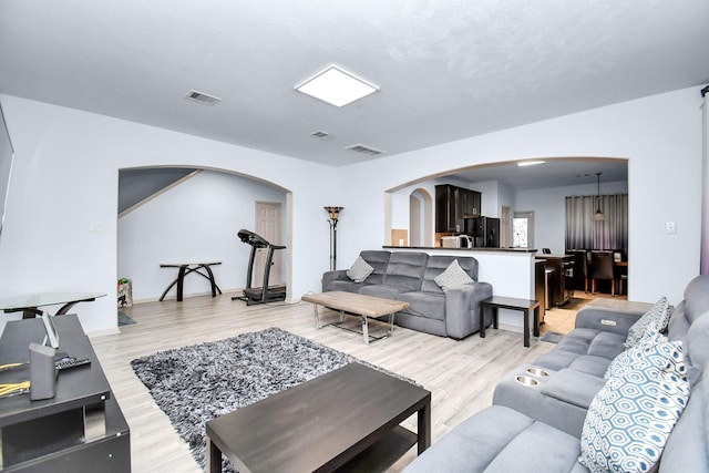 living room featuring light wood-type flooring, arched walkways, and visible vents