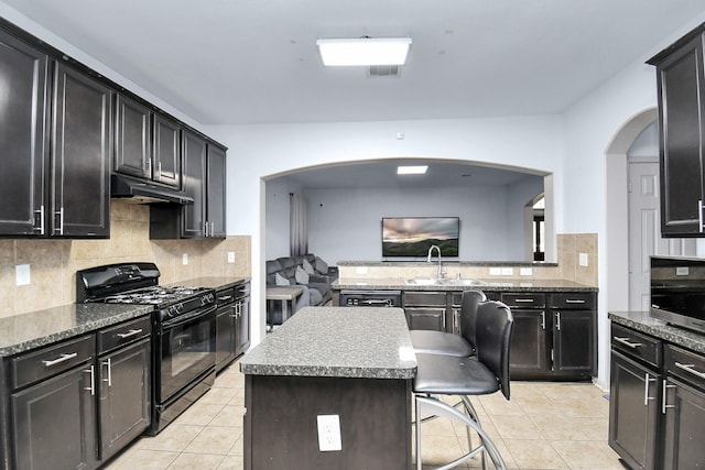 kitchen with light tile patterned floors, black gas range, under cabinet range hood, a breakfast bar, and a center island