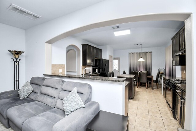 kitchen featuring arched walkways, light tile patterned floors, visible vents, dark stone counters, and black appliances