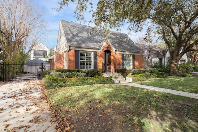 view of front of home featuring a gate, brick siding, a front lawn, and roof with shingles