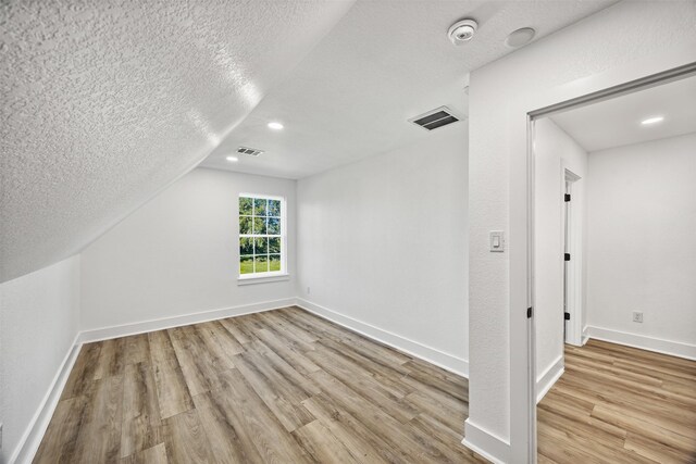 additional living space with a textured ceiling, wood finished floors, visible vents, and baseboards