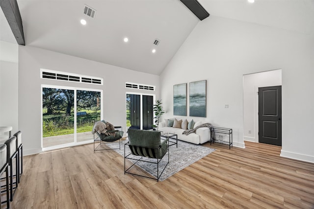 living area featuring high vaulted ceiling, light wood finished floors, visible vents, and beam ceiling