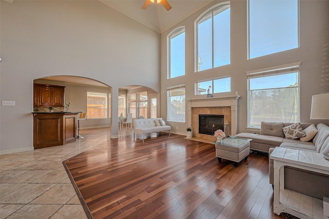 unfurnished living room featuring arched walkways, a tiled fireplace, light wood-style flooring, and baseboards