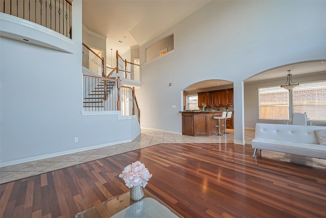 unfurnished living room featuring light tile patterned floors, arched walkways, a towering ceiling, baseboards, and stairs