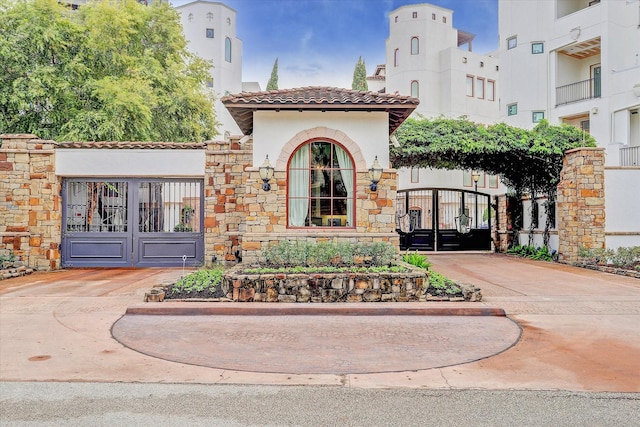 exterior space with stone siding, a tile roof, a gate, and stucco siding