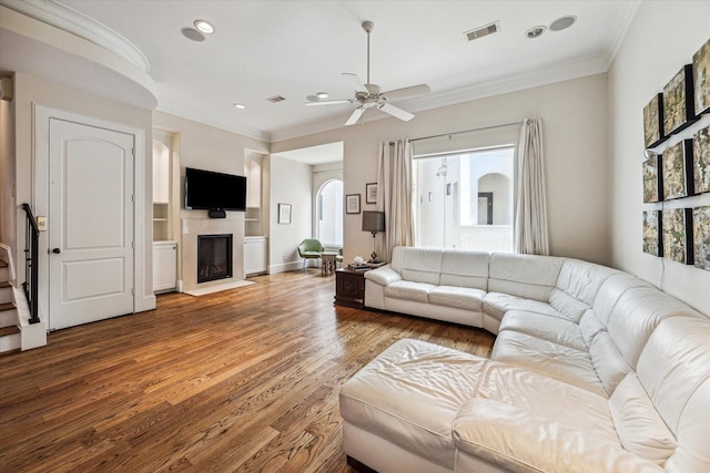 living area featuring a fireplace with flush hearth, visible vents, ornamental molding, and wood finished floors