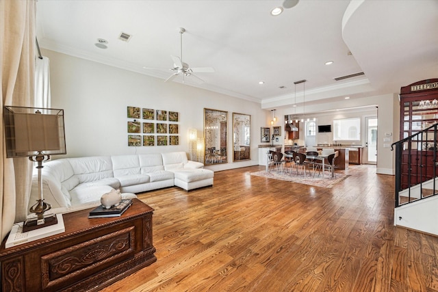 living area with ornamental molding, wood finished floors, visible vents, and stairs