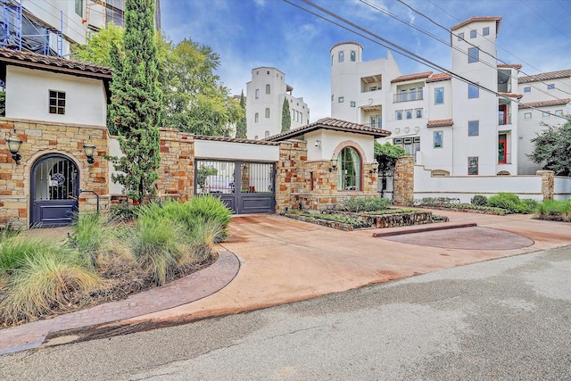 exterior space featuring stone siding, a gate, stucco siding, and a tiled roof