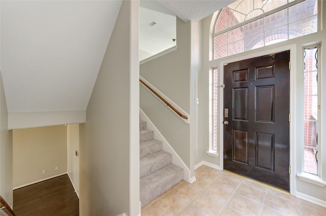 foyer featuring lofted ceiling, light tile patterned floors, baseboards, and stairs