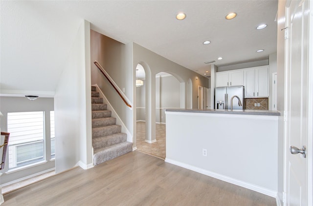 kitchen featuring arched walkways, light wood-style flooring, white cabinets, stainless steel refrigerator with ice dispenser, and backsplash