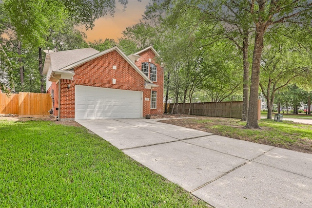 view of front of house featuring brick siding, fence, a lawn, driveway, and an attached garage