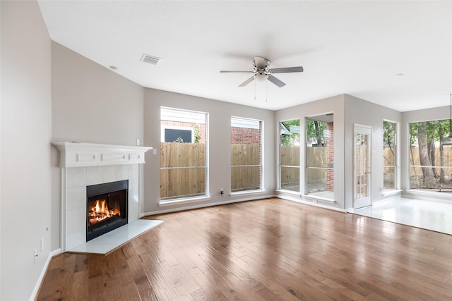 unfurnished living room with a tiled fireplace, visible vents, a healthy amount of sunlight, and wood finished floors