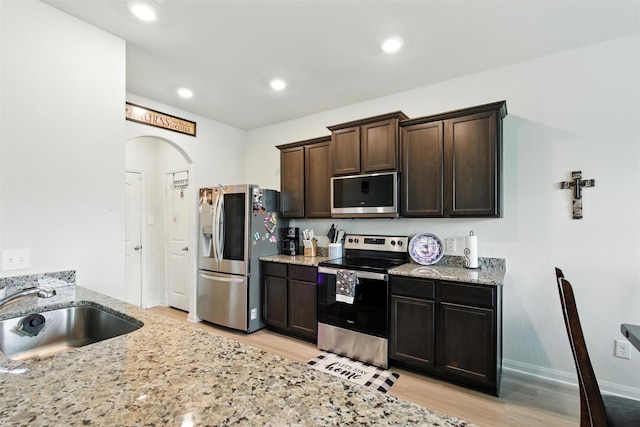 22052 Angelico Dr, Magnolia, TX 77355 - kitchen with appliances with stainless steel finishes, dark brown cabinets, light wood-style floors, light stone counters, and recessed lighting