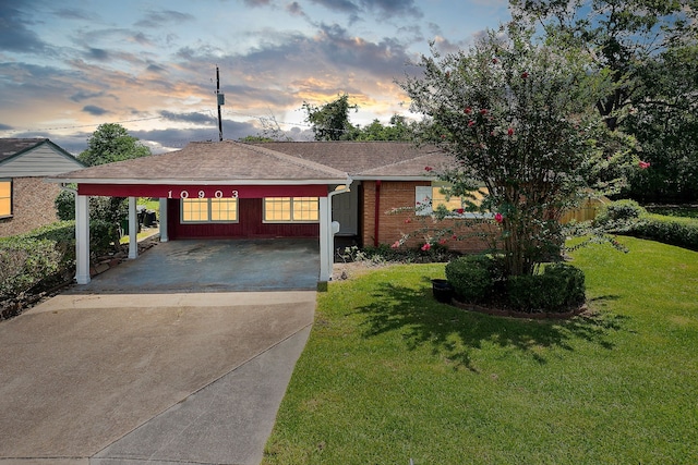 ranch-style house featuring driveway, a shingled roof, a yard, a carport, and brick siding