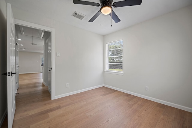 empty room featuring attic access, visible vents, light wood-style flooring, and baseboards