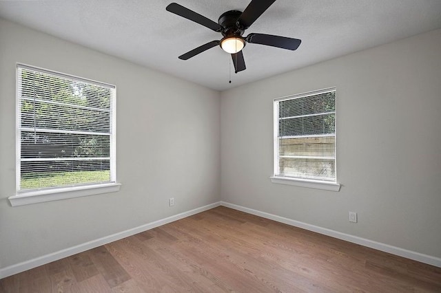 empty room featuring a healthy amount of sunlight, ceiling fan, baseboards, and wood finished floors