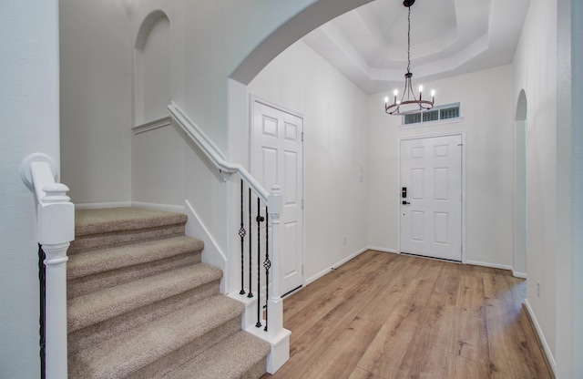 entrance foyer with a tray ceiling, arched walkways, light wood-style floors, an inviting chandelier, and stairs