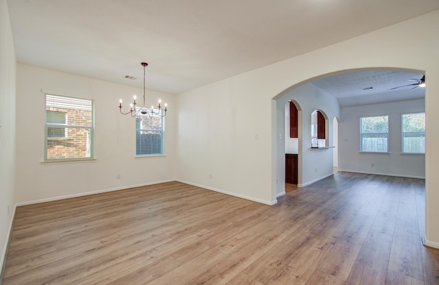 spare room with light wood-style flooring, ceiling fan with notable chandelier, arched walkways, and a healthy amount of sunlight