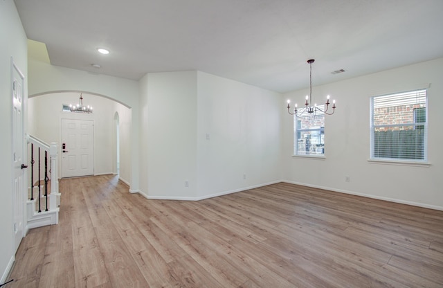 unfurnished room featuring a notable chandelier, light wood-style floors, arched walkways, and baseboards