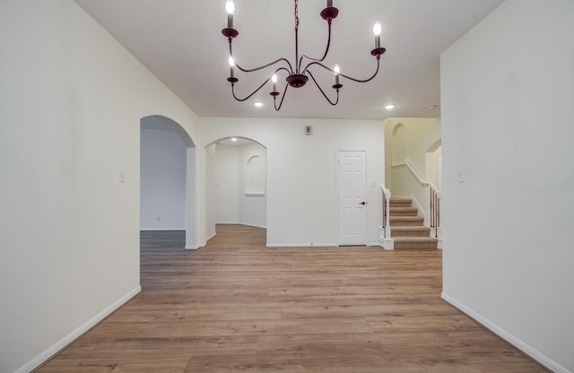 unfurnished dining area with light wood-style flooring, baseboards, arched walkways, and a chandelier