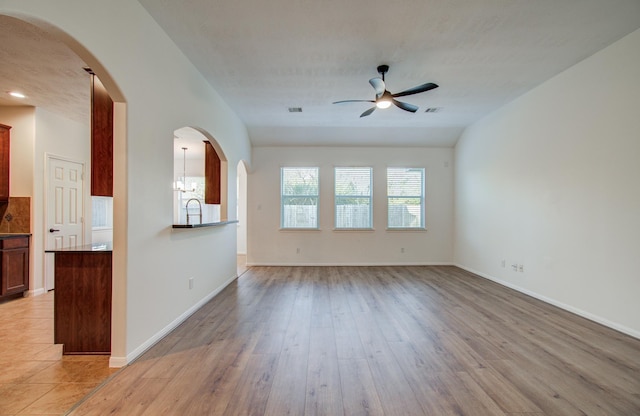 unfurnished living room featuring a sink, arched walkways, a ceiling fan, and light wood finished floors