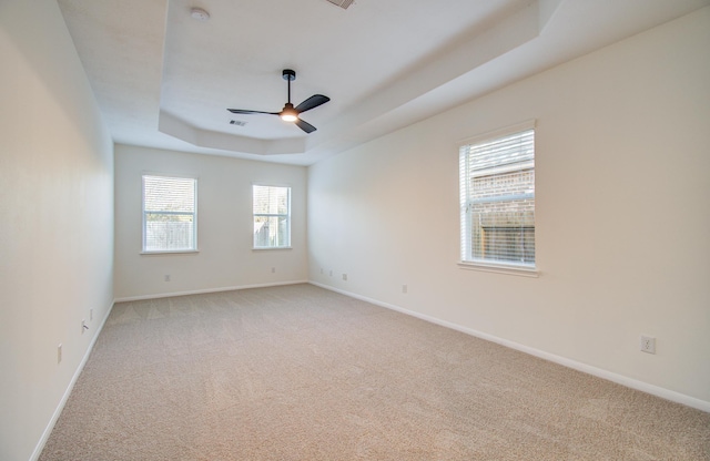 empty room with baseboards, a raised ceiling, light colored carpet, and ceiling fan