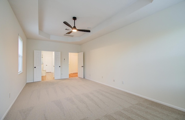 unfurnished bedroom with light carpet, connected bathroom, a raised ceiling, and baseboards