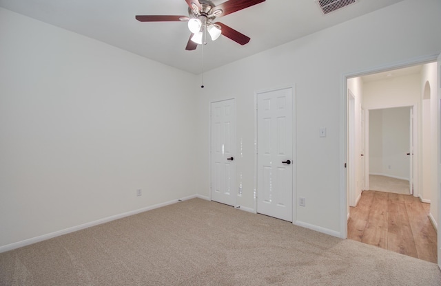 unfurnished bedroom featuring light carpet, visible vents, two closets, and baseboards