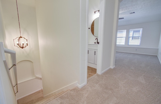 hallway with visible vents, baseboards, a notable chandelier, and carpet flooring