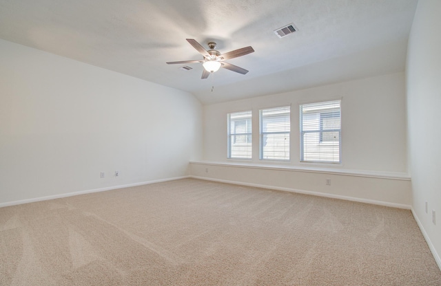 spare room featuring a ceiling fan, visible vents, baseboards, lofted ceiling, and light colored carpet