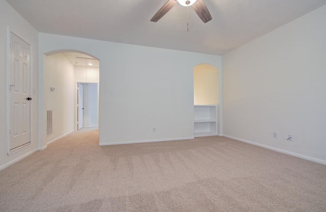 unfurnished room featuring baseboards, a ceiling fan, arched walkways, and light carpet